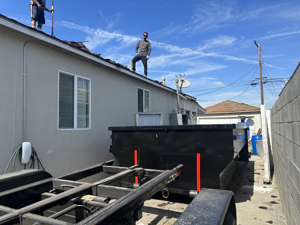 Workers standing on a roof and a large black dumpster trailer in a narrow alley, Dumpster Rental Services