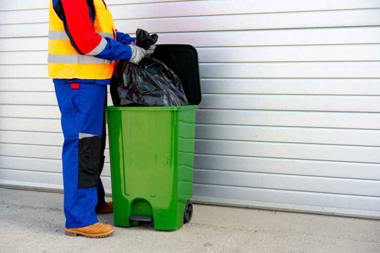 Janitor takes garbage out of trash container outdoors in the street