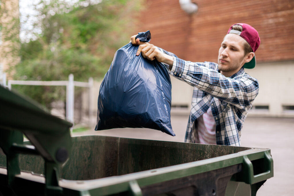 male dumping waste package into a big trash bin container