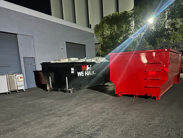 Two red dumpsters sit in a dimly lit parking lot at night, surrounded by shadows and sparse lighting.